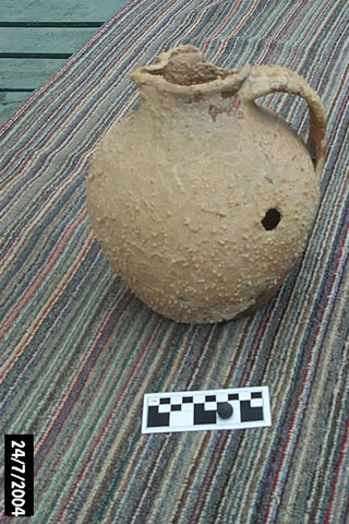A French Earthenware jug, dredged up in Crouse Harbour, 17th-or 18th-century. The jug was damaged by a musket shot. Notice the musket ball, found inside the jug, visible on the scale bar.